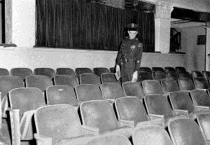 1963 Police officer walking through theatre seats